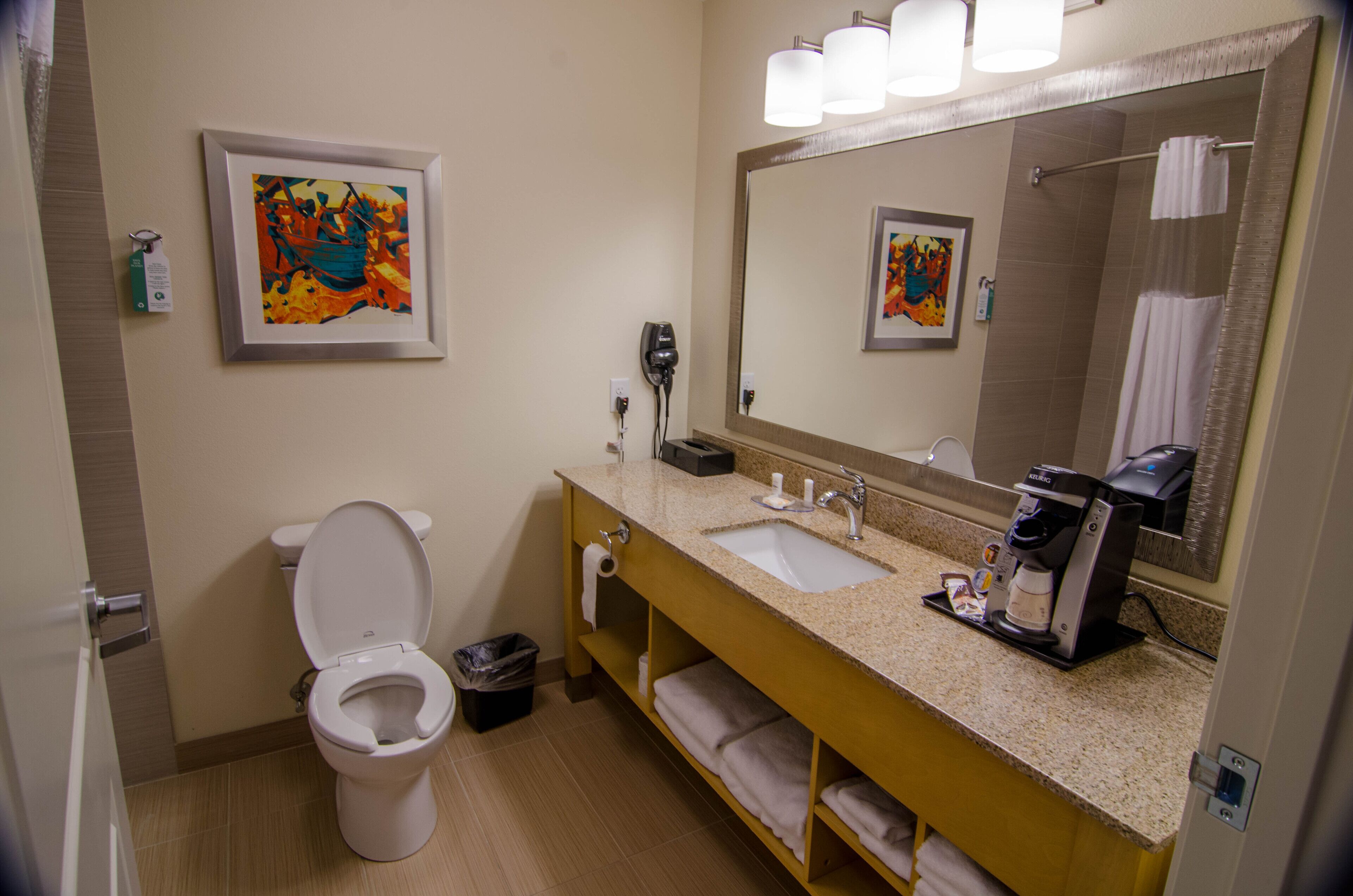 Een badkamer met toilet, wastafel en spiegel. Handdoeken en een prullenbak zijn aanwezig.