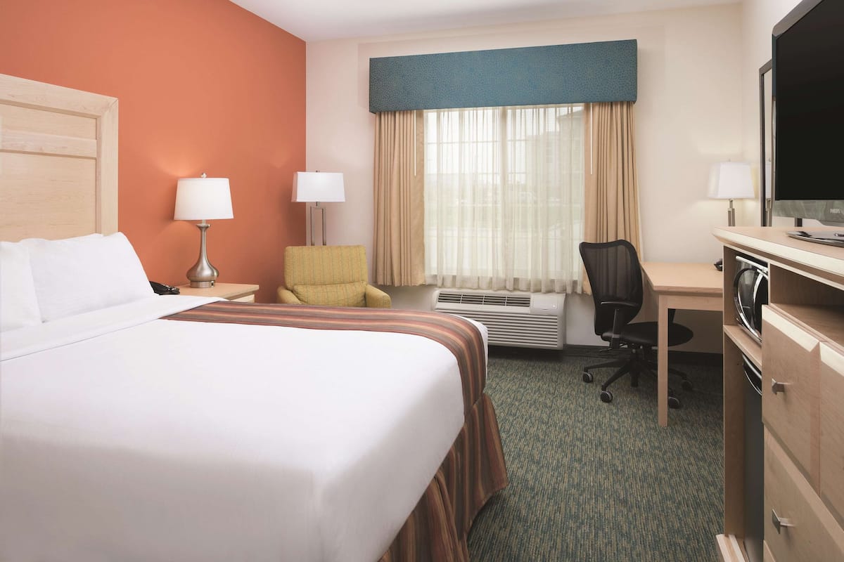 Una habitación de hotel con cama, escritorio, silla, dos lámparas, aire acondicionado y televisión.
