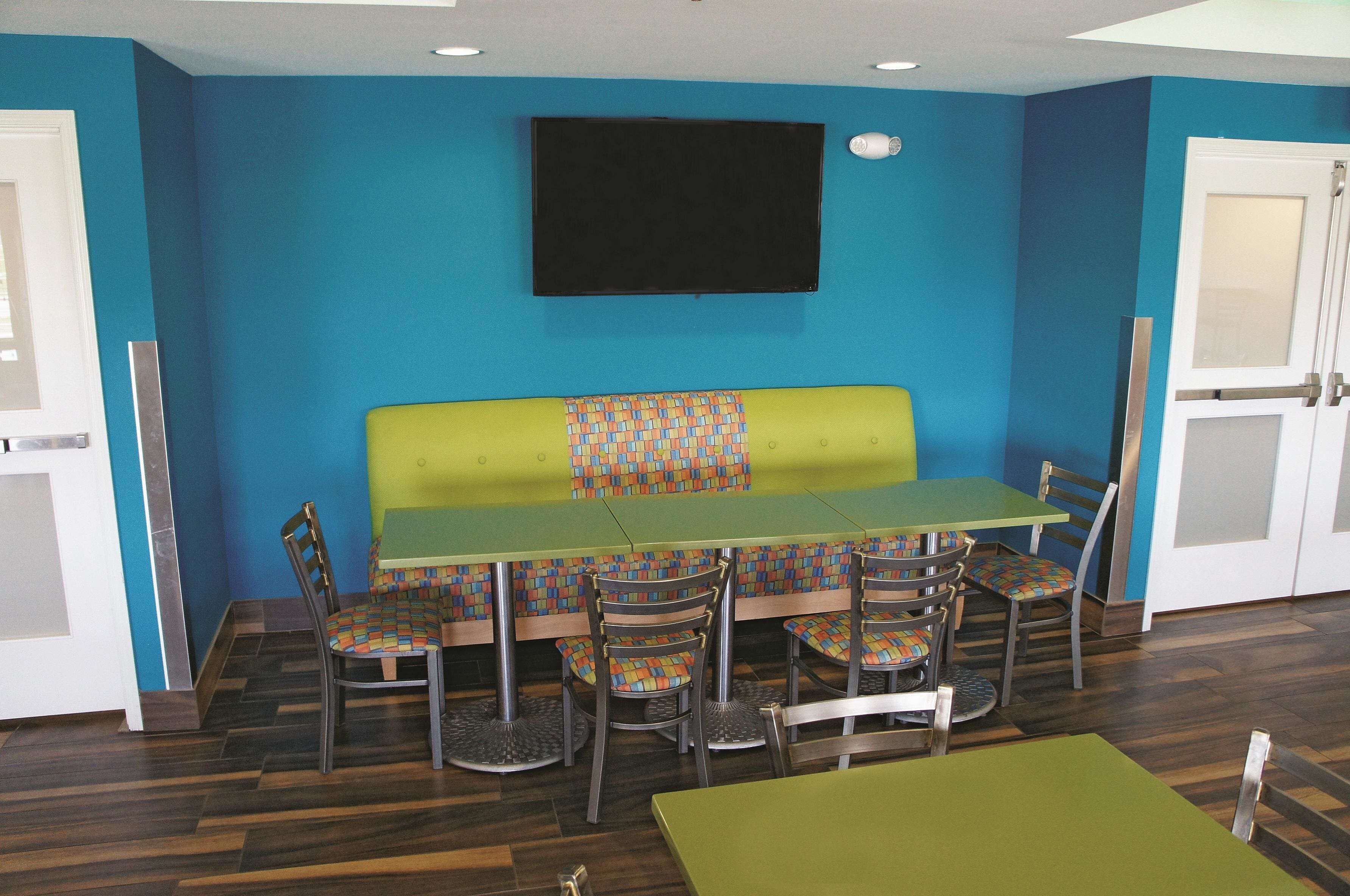 A room with a green sofa, multiple chairs, a table, and a TV mounted on the wall.