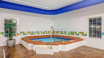 Une pièce avec un jacuzzi, une plante en pot et un mur recouvert de carreaux colorés.