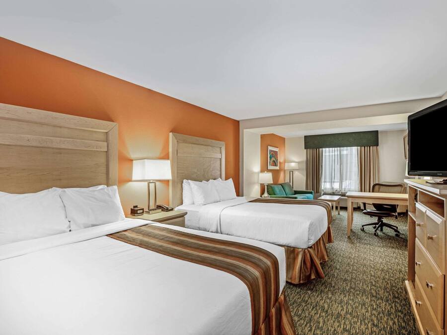 Quarto de hotel com duas camas, uma escrivaninha, uma televisão e uma cadeira.