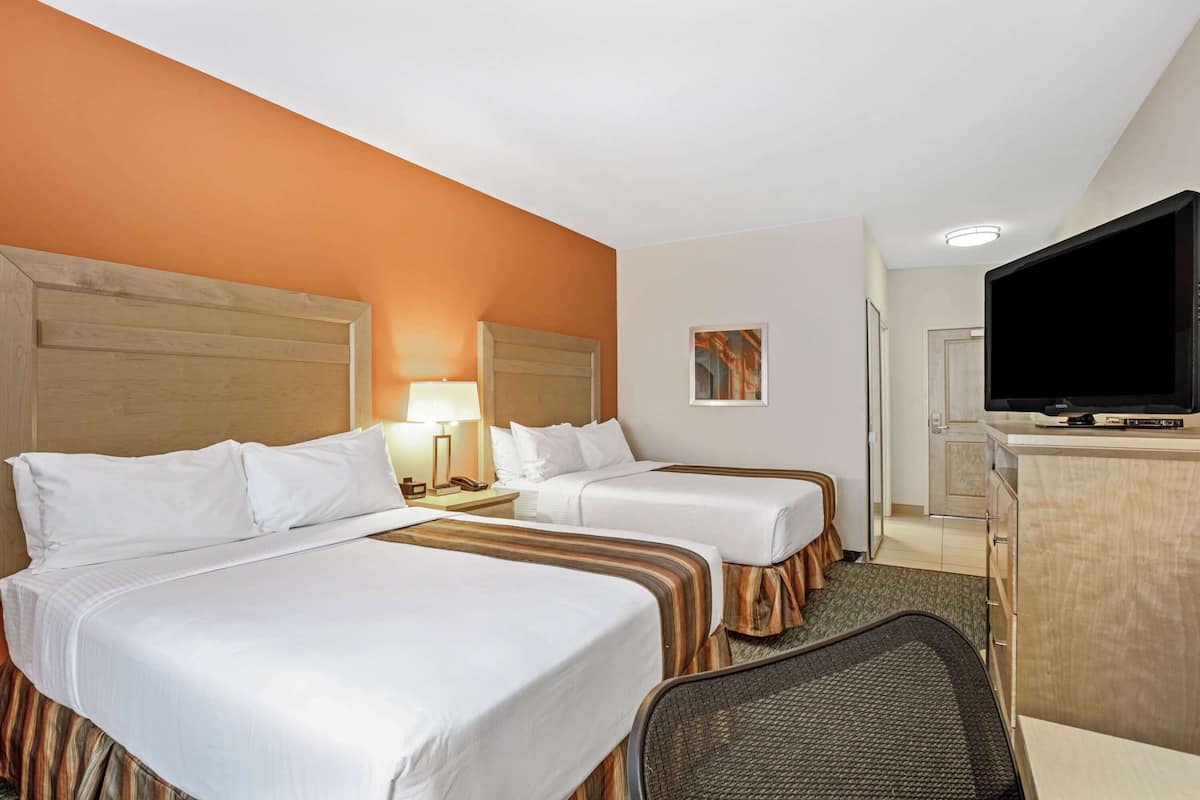Habitación de hotel con dos camas, televisión, escritorio y lámpara.