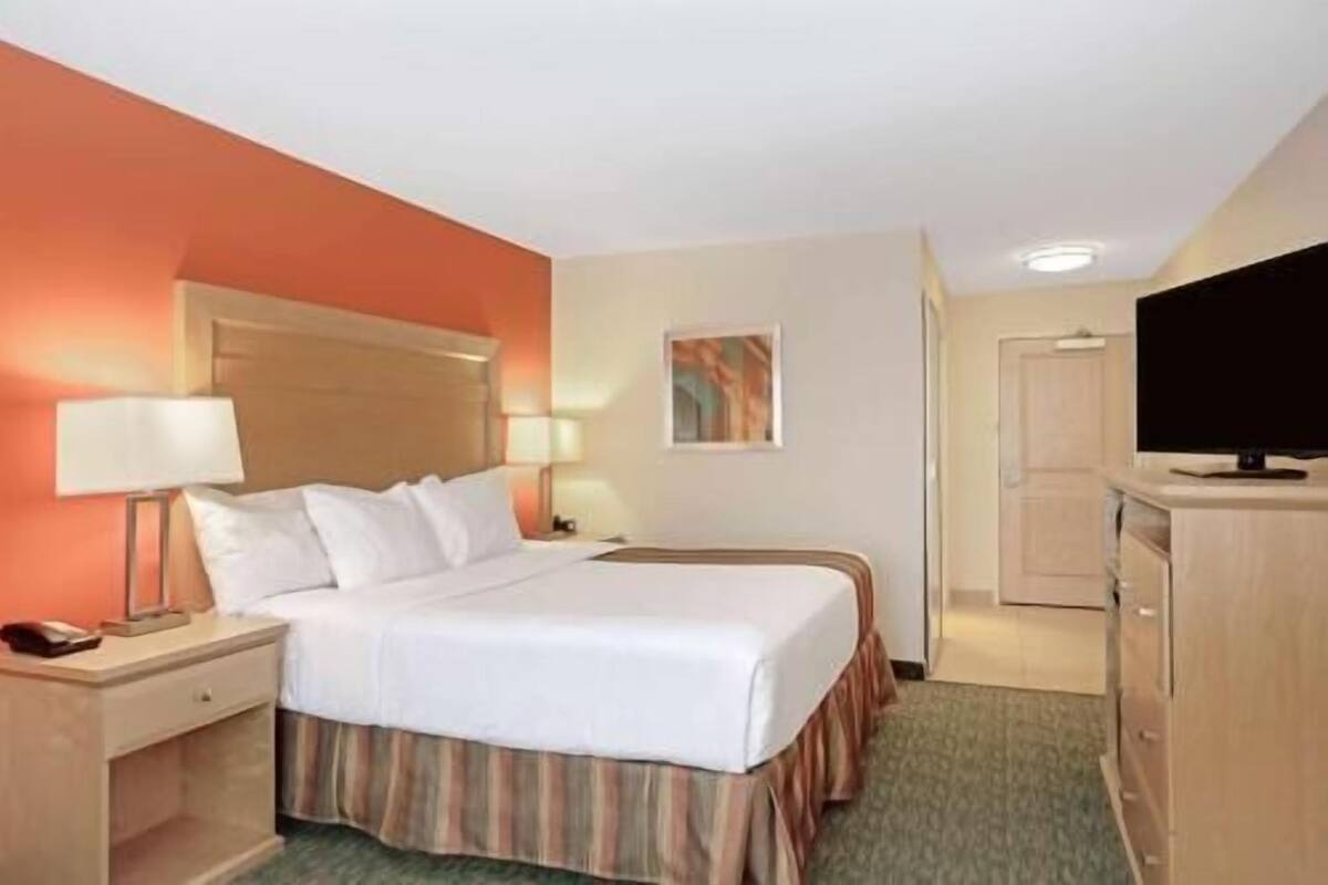 Una habitación de hotel con cama, mesitas de noche, televisión y puerta.