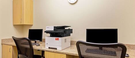 A small office with two computer monitors, a printer, and two office chairs.