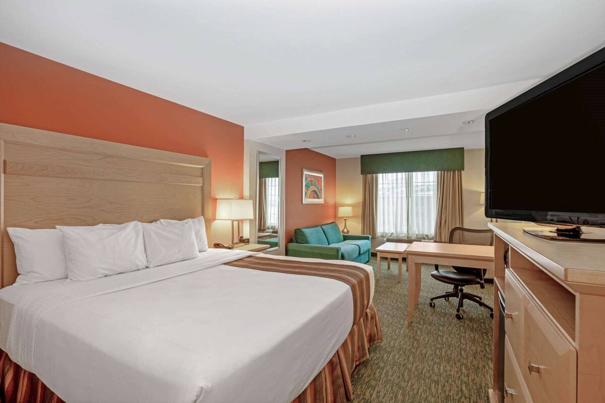 Una habitación de hotel con una cama grande, un escritorio, una silla, un televisor y un sofá.