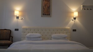 A hotel room with a tufted headboard, two bedside lamps, a framed artwork above the bed, and a chair to the left. - Guesthouse Pickery (Bruges)