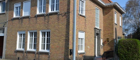 Un bâtiment de deux étages en briques, avec des fenêtres à cadre blanc et un toit recouvert de tuiles rouges.