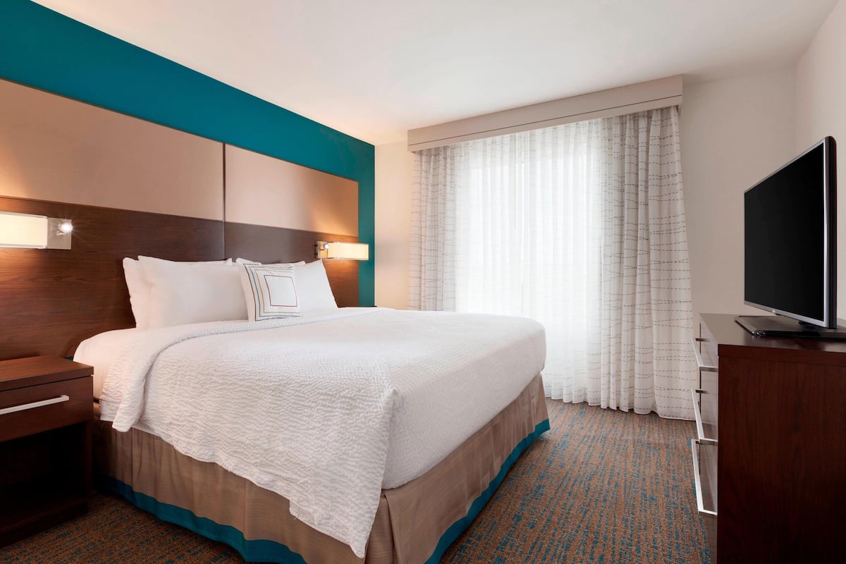 A hotel room with a large bed, a TV, a nightstand, and a window with curtains.