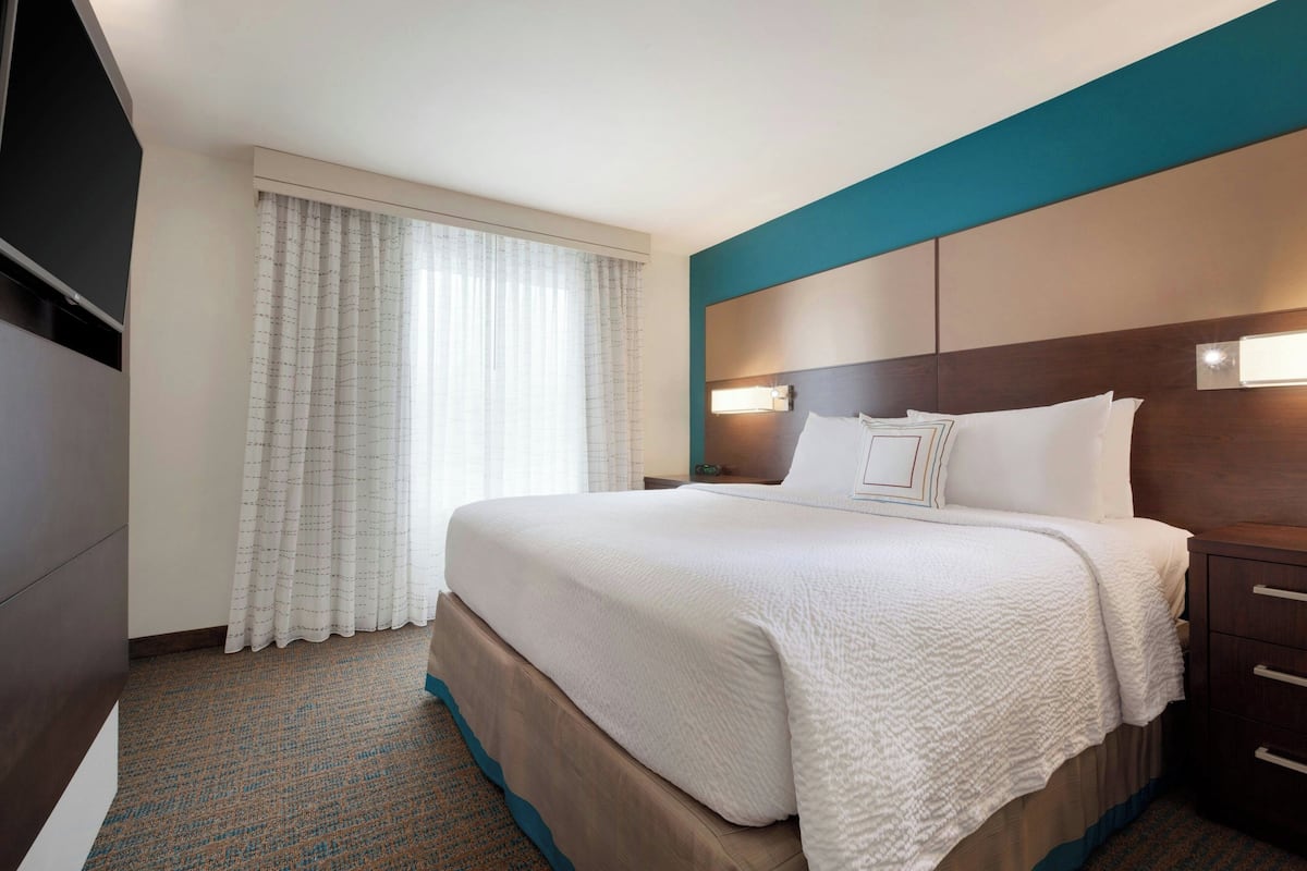 A hotel room with a large bed, a nightstand, a TV, and a window with curtains.