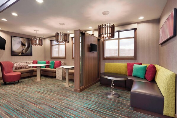 A modern hotel room with a sectional sofa, a round table, and a TV.