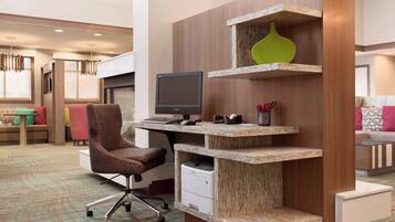 A modern office space with a wooden desk, a computer, and a printer. There is a comfortable chair and a sofa in the background.