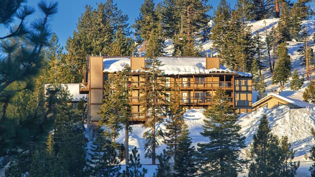 Eine Lodge mit mehreren Stockwerken, umgeben von schneebedeckten Bergen und dichten Kiefernwäldern.