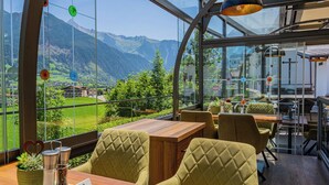 Un restaurante con vistas a las montañas, con mesas de madera y sillas acolchadas.
