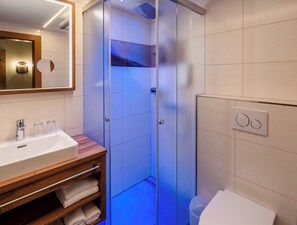 Un baño moderno con ducha envuelta en vidrio, tocador de madera con lavabo y espejo.
