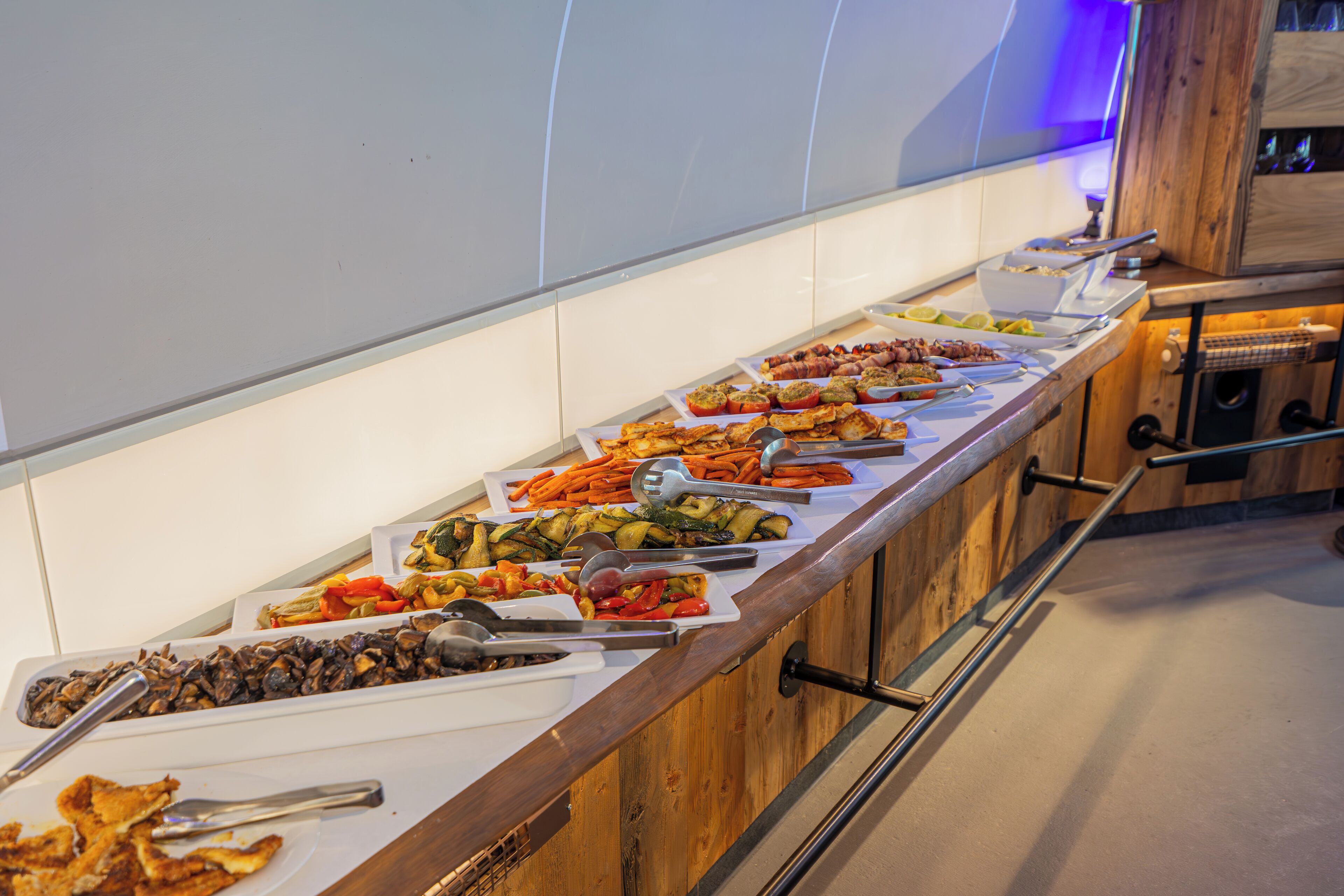 A buffet with various dishes including vegetables, meats, and cheeses.