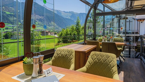 Un restaurante con vistas a las montañas, mesas de madera y sillas tapizadas de verde.