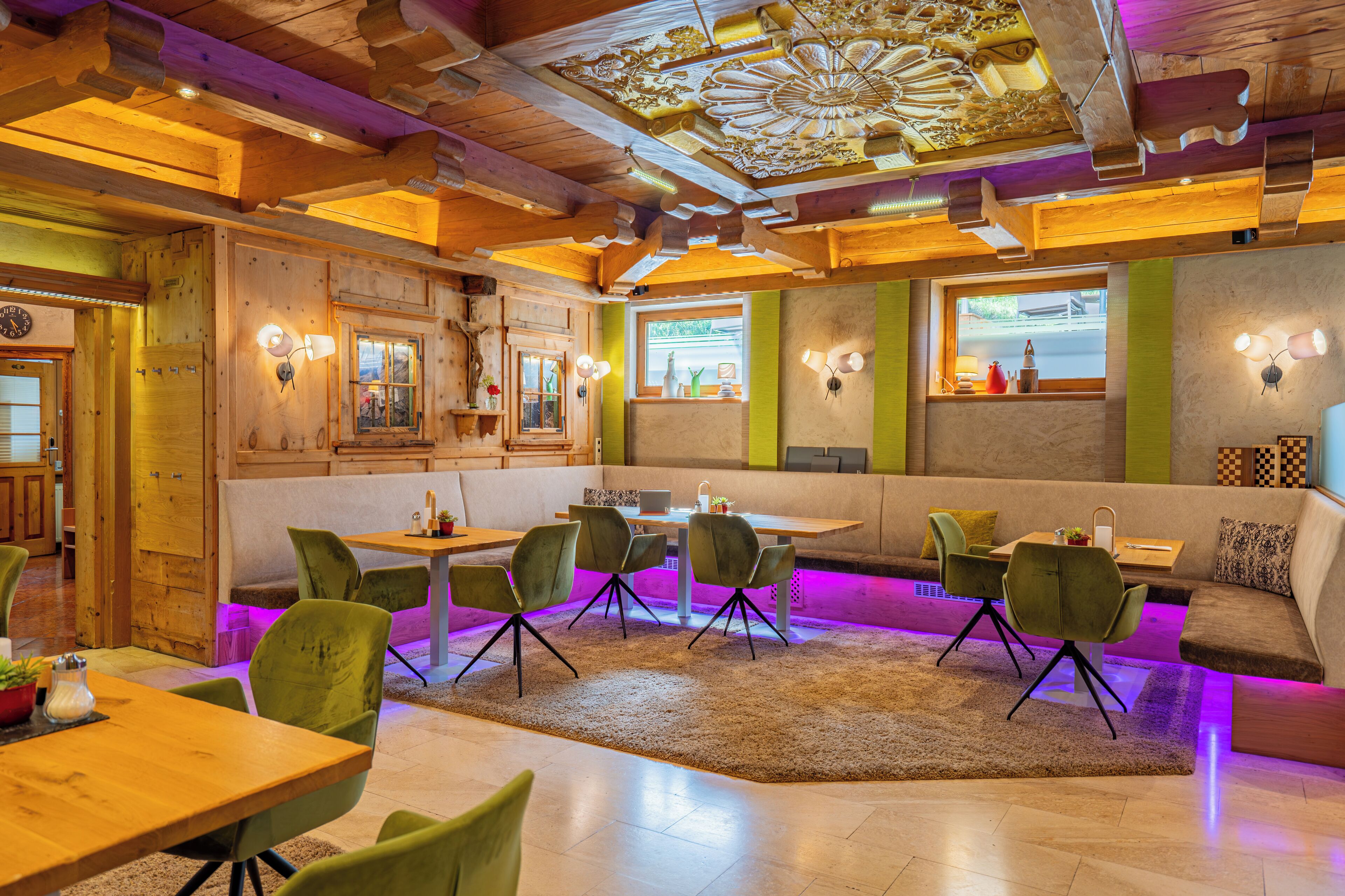 A cozy restaurant with wooden interiors, green upholstered chairs, and a central dining table.