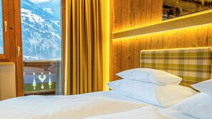 Un dormitorio con cabecera de madera, cama con ropa de cama blanca y vista a montañas nevadas a través de una ventana.