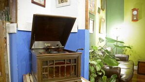 Ein altes Radio auf einem Holzständer, ein grünes Sofa und eine große Pflanze in einem Zimmer mit blauen und grünen Wänden.