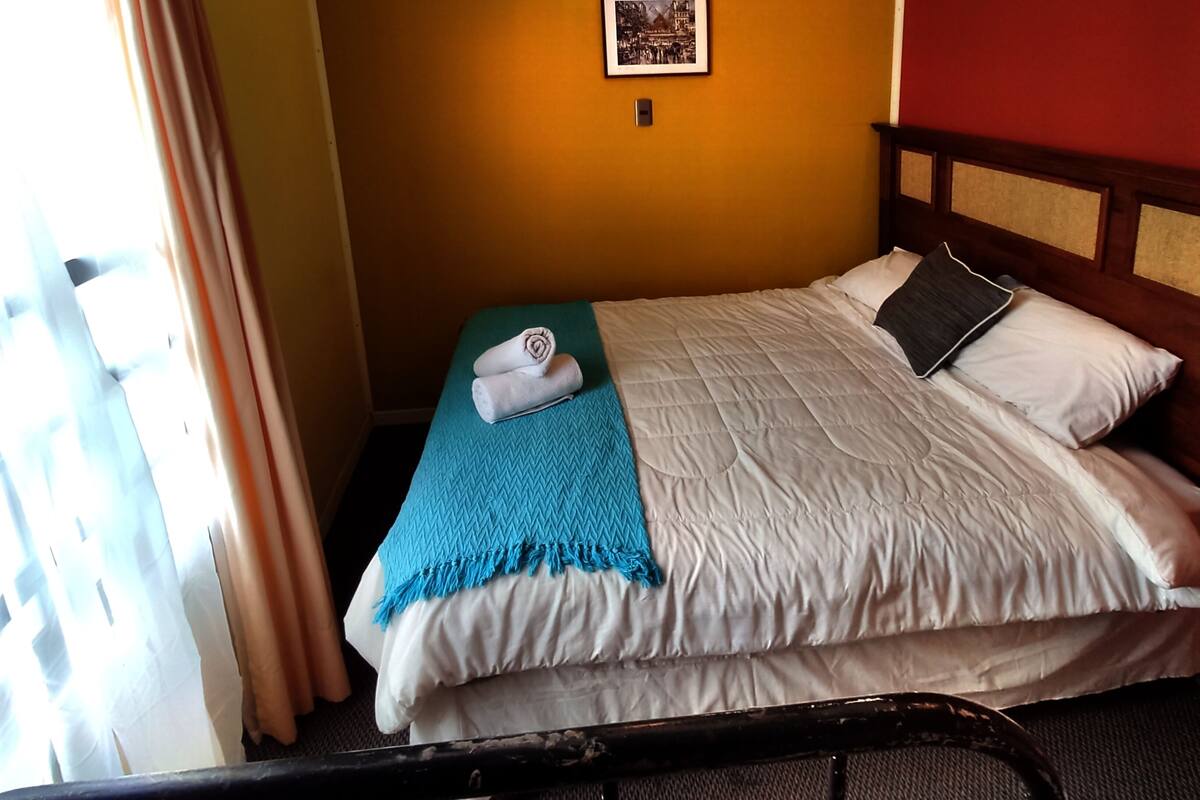 A hotel room with a bed, a blue throw blanket, and a framed picture on the wall.