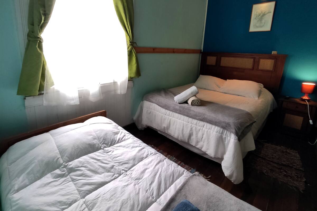 A room with two beds, a nightstand with a lamp, and a window with curtains.