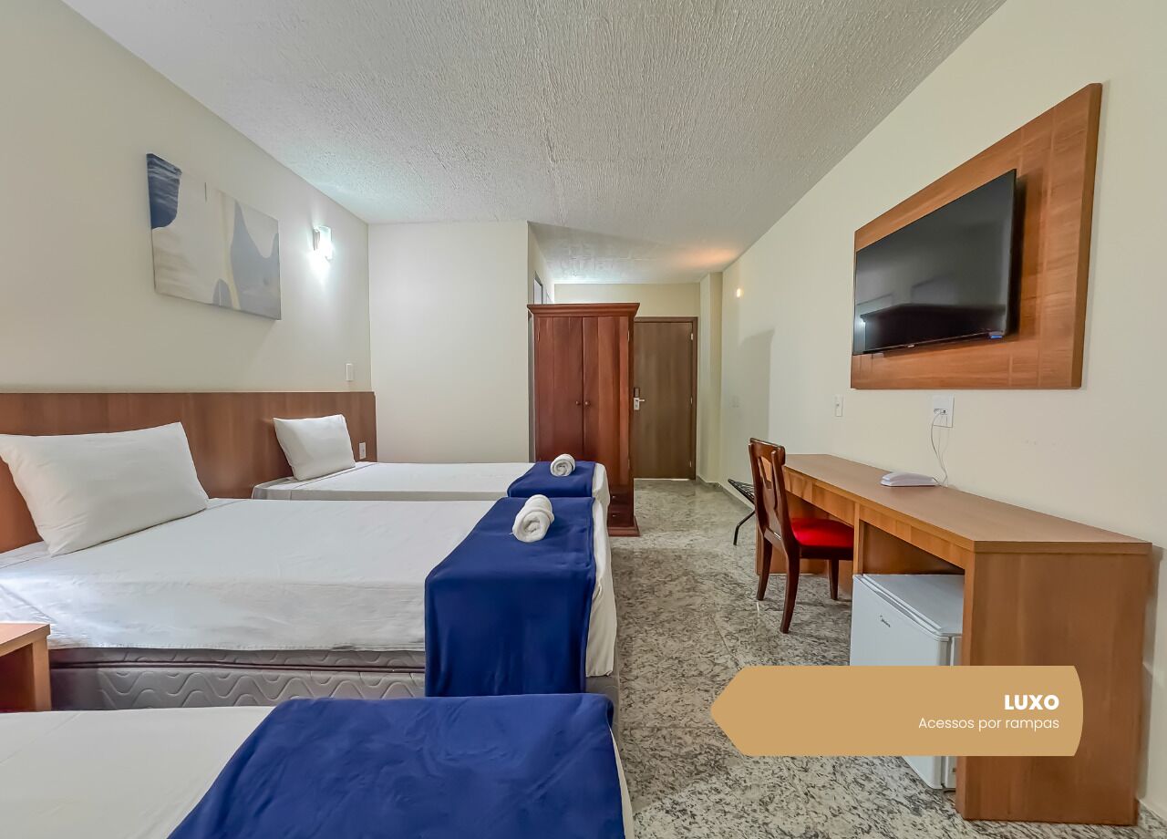 Habitación de hotel con tres camas, un escritorio, televisión y minibar.