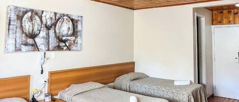 Habitación de hotel con dos camas individuales, un cabecero de madera, un cuadro en la pared y una puerta que da a otra habitación.