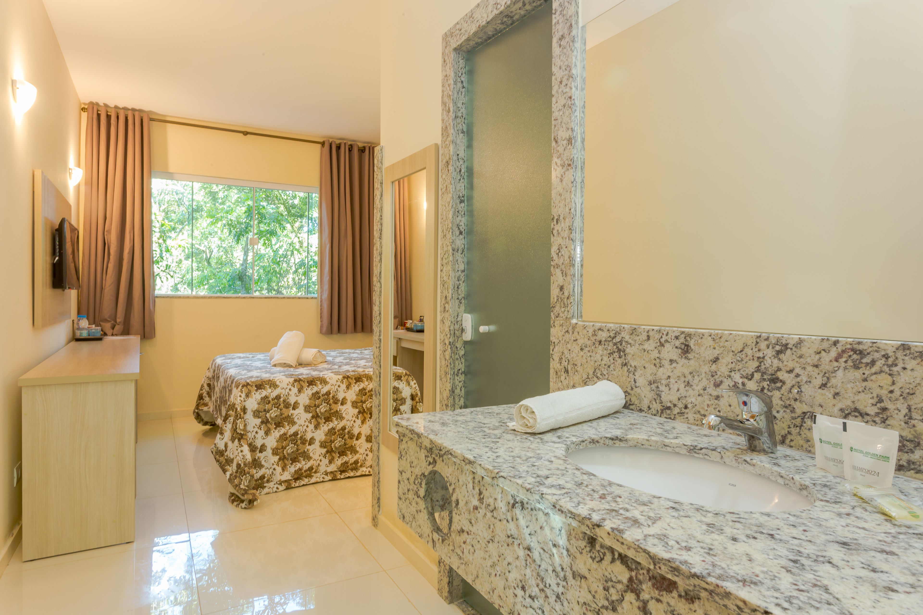 A hotel room with a bed, a bathroom with a sink and mirror, and a window with curtains.