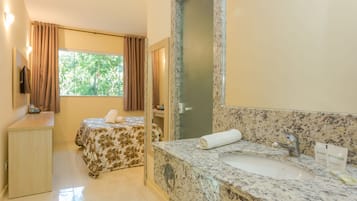 A hotel room with a bed, a bathroom with a sink and mirror, and a window with curtains.
