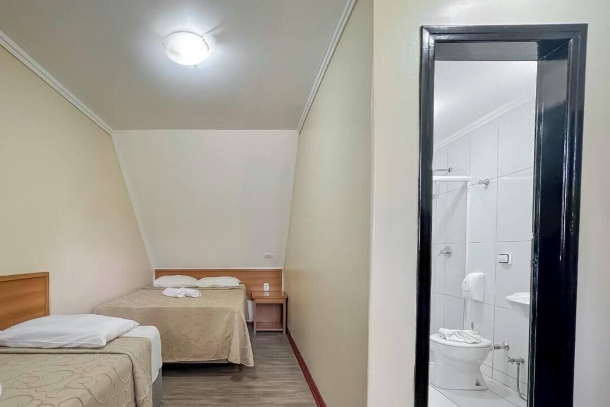 A hotel room with two beds, a wooden headboard, a bedside table, and a bathroom with a toilet and sink.