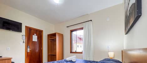 Ein Hotelzimmer mit Bett, Schreibtisch, Telefon, einem Fenster mit Vorhängen und einem Bild an der Wand.