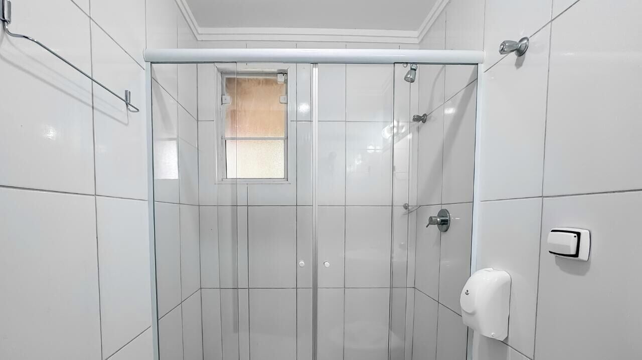 A modern bathroom with a glass-enclosed shower, white tiled walls, a small window, and a hand soap dispenser.