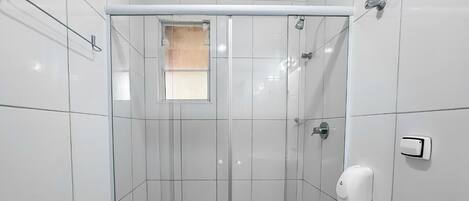 A modern bathroom with a glass-enclosed shower, white tiled walls, a small window, and a hand soap dispenser.