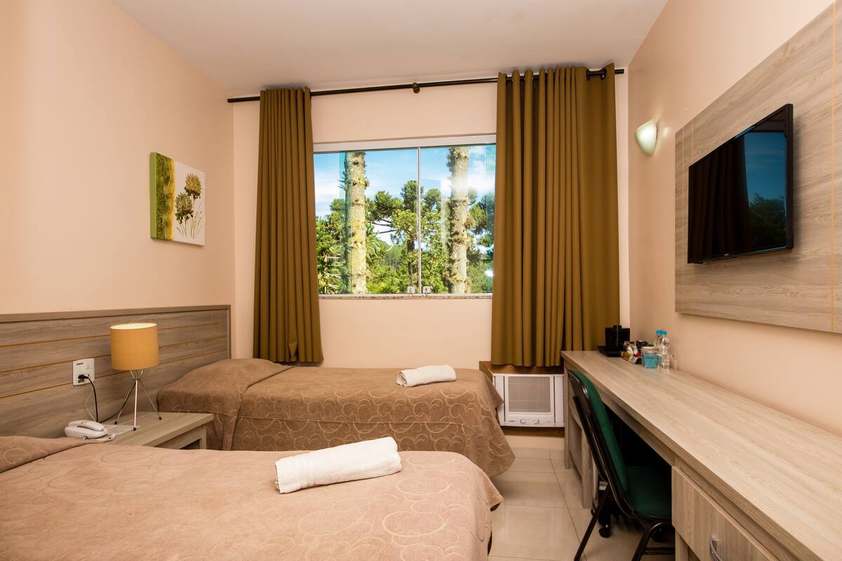 A hotel room with two beds, a desk, a TV, a window with curtains, and a painting on the wall.
