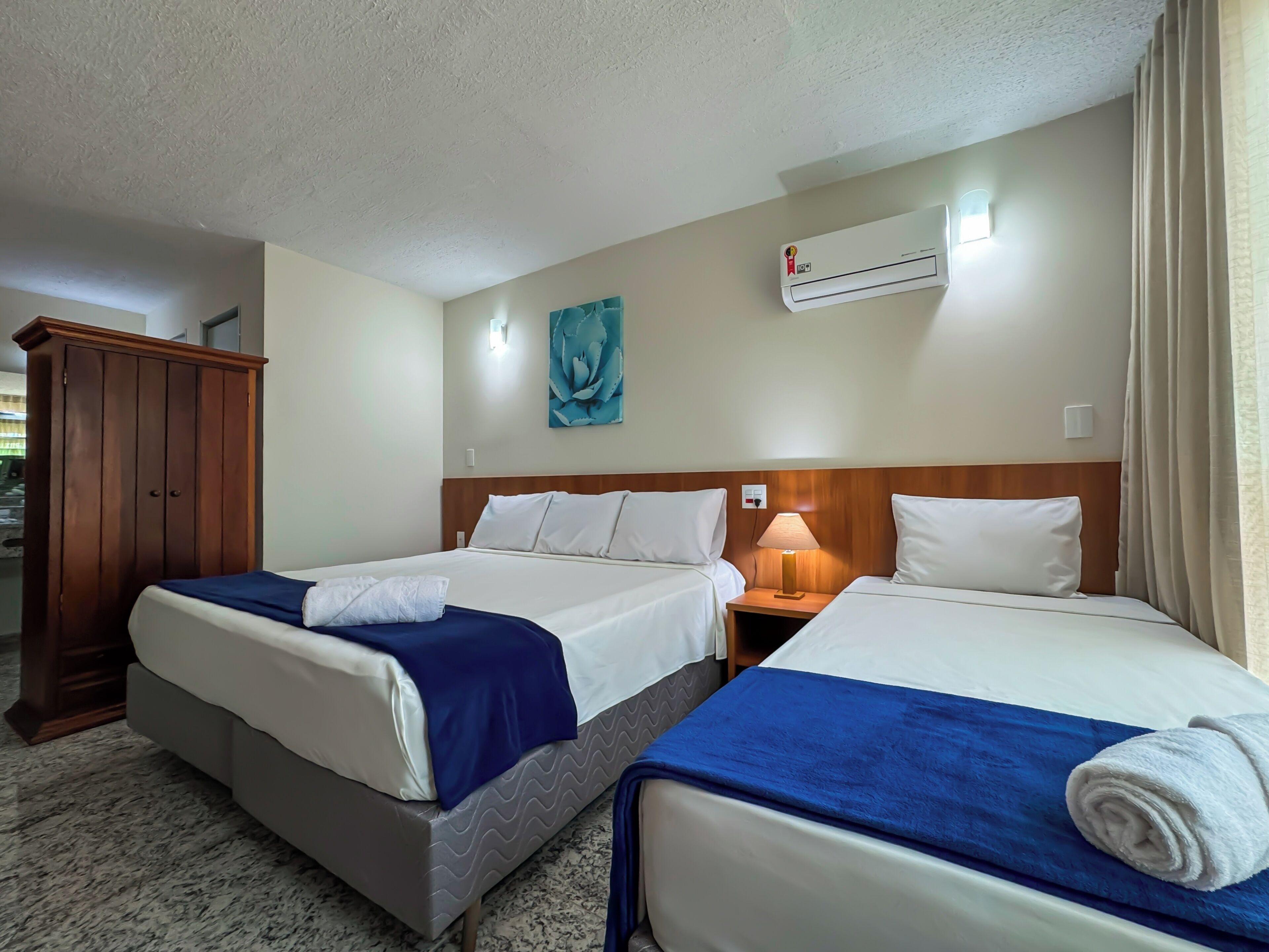 Habitación de hotel con dos camas, un armario, un equipo de aire acondicionado, una lámpara y un cuadro en la pared.