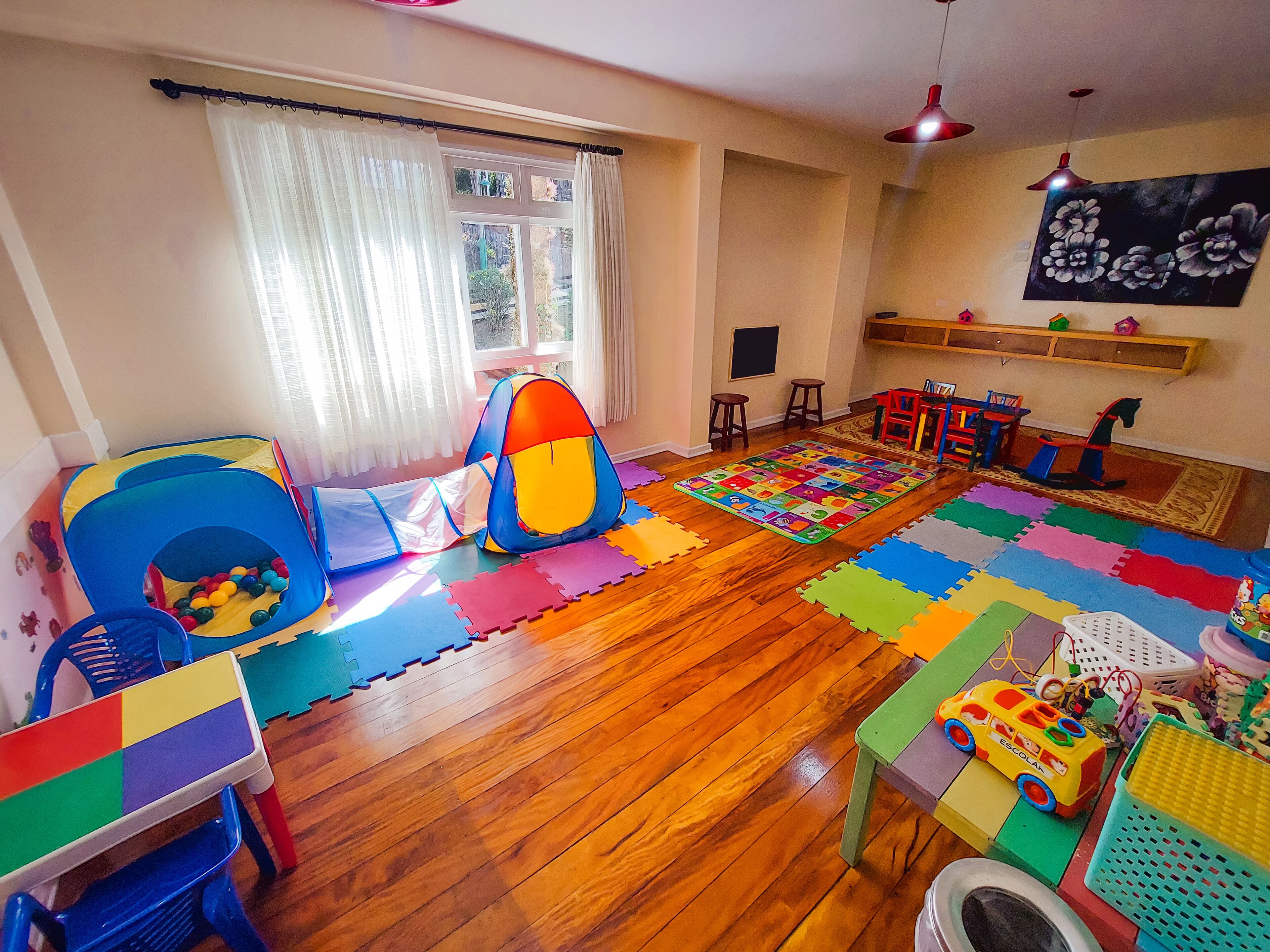 A playroom with a wooden floor, colorful play mats, a play tent, and a toy car.
