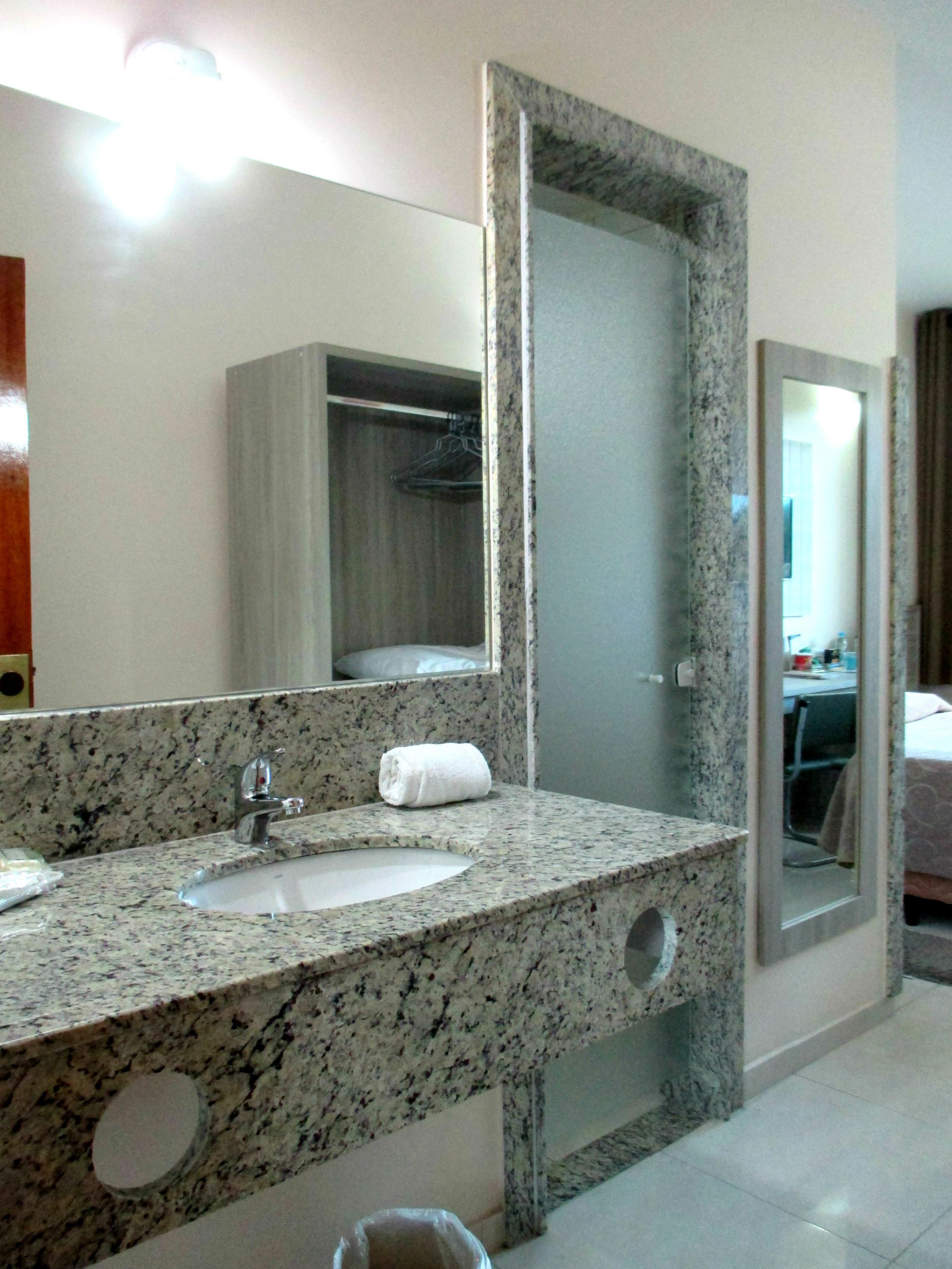 Un baño con encimera de granito, lavamanos y un espejo grande.