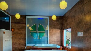 A modern bathroom with a wooden bathtub, a large mirror, and a unique green and white wall art piece.
