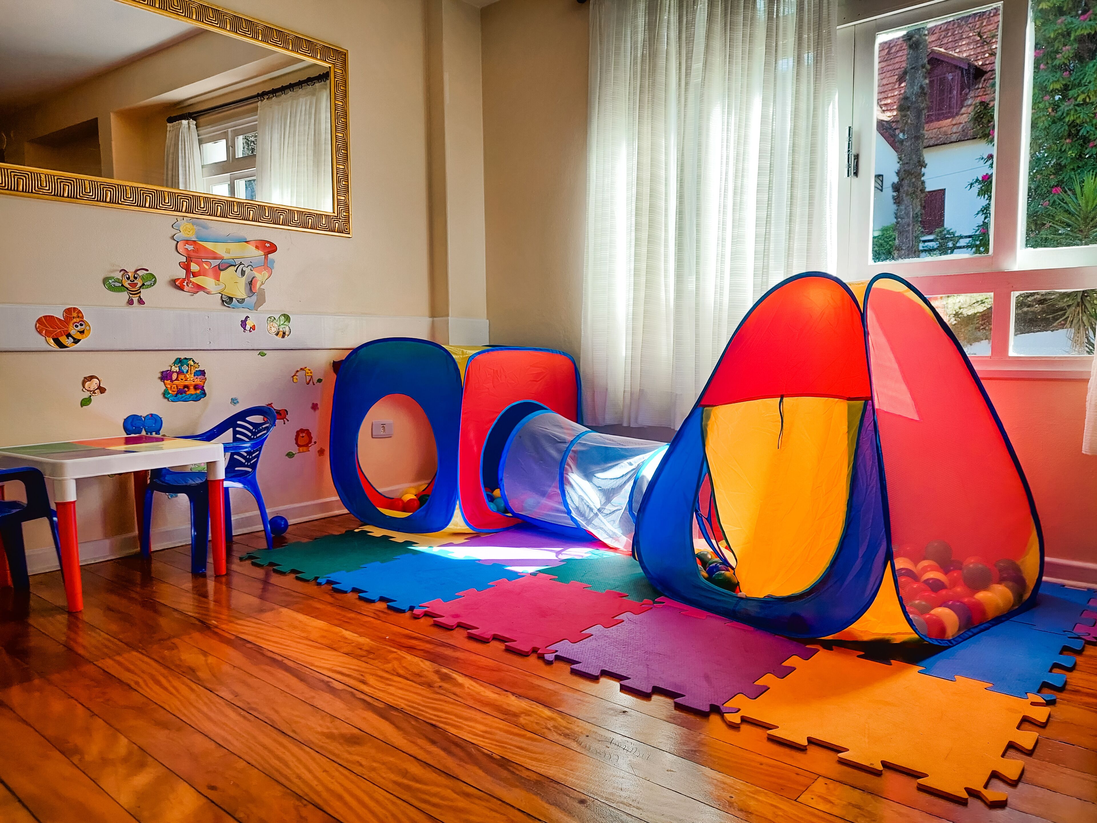 A child's play area with a tunnel, colorful mats, and a table with chairs.