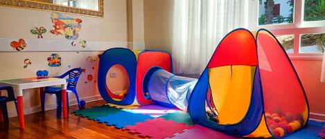 A child's play area with a tunnel, colorful mats, and a table with chairs.
