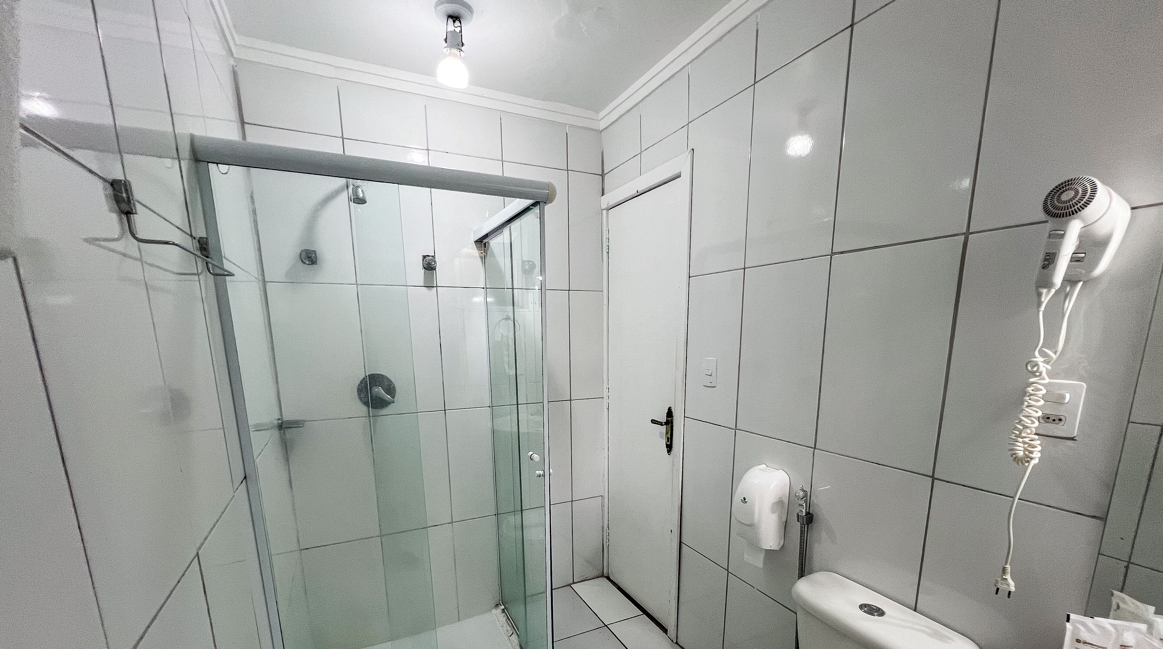 Un baño moderno con cabina de ducha acristalada, un secador de pelo en la pared y un inodoro.