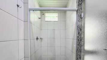 Ducha con azulejos blancos, puerta de cristal y una ventana pequeña.