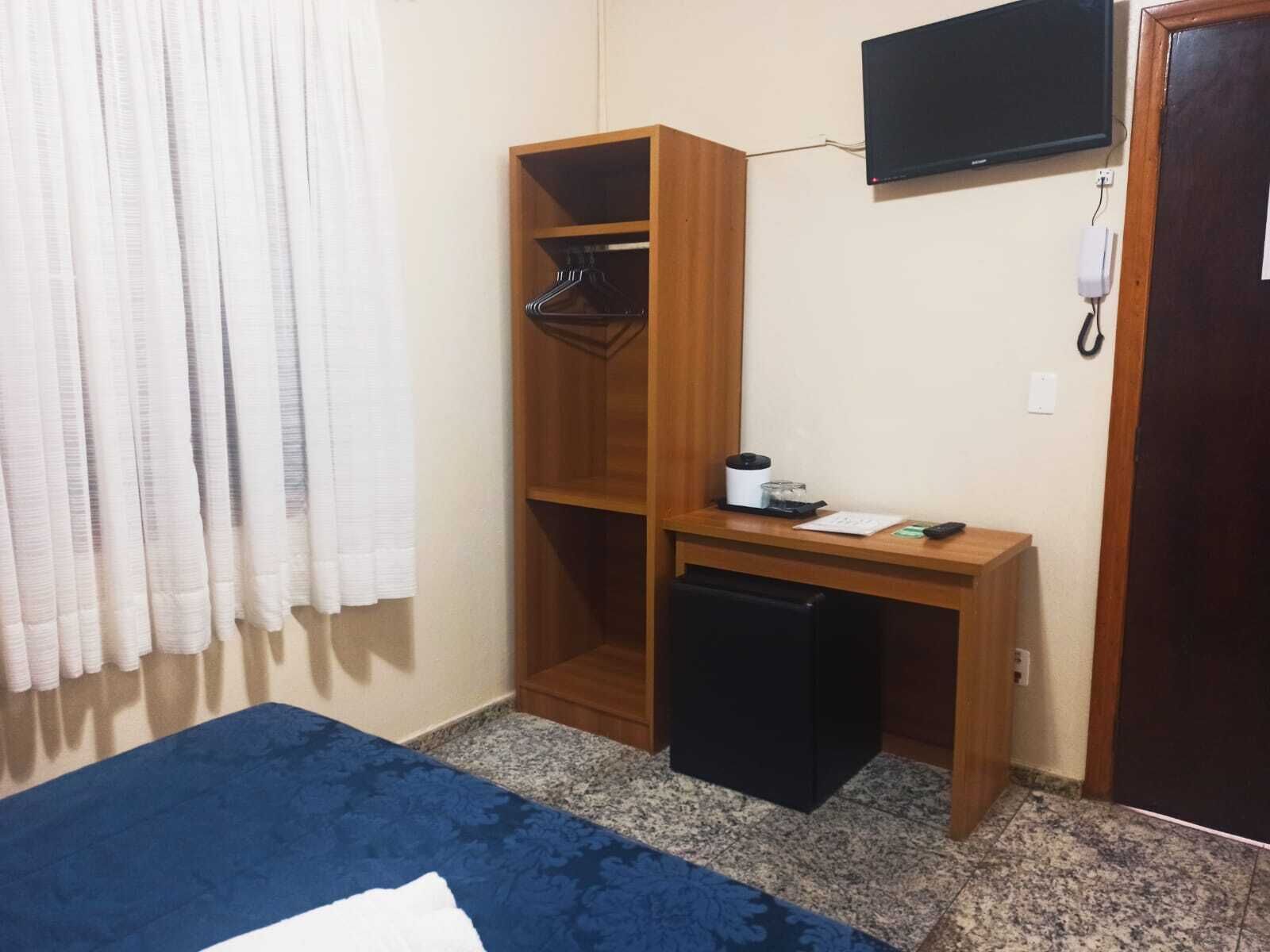 Ένα μικρό δωμάτιο με ένα κρεβάτι, ένα γραφείο, μια ντουλάπα, μια τηλεόραση και μια πόρτα.