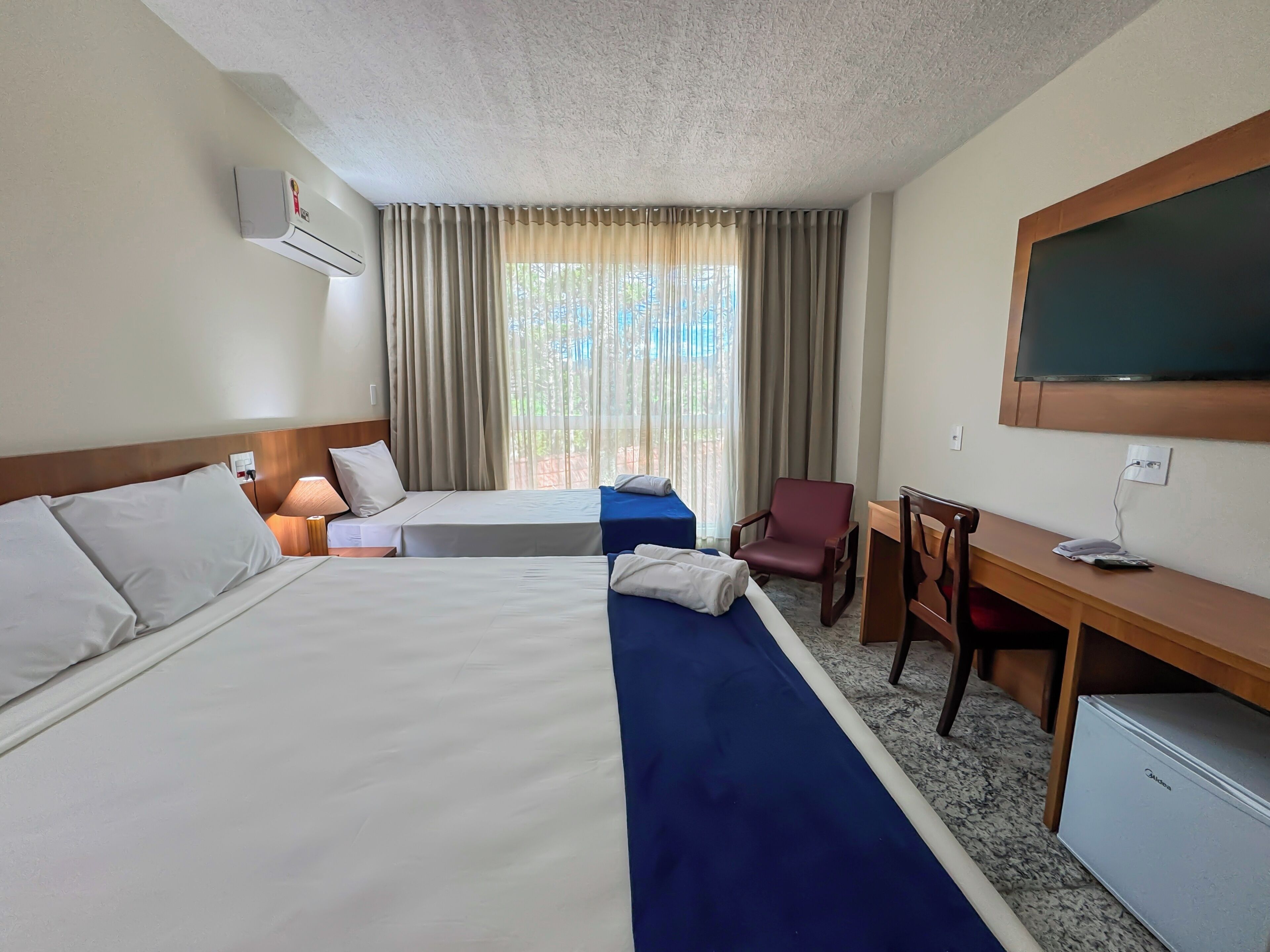 A hotel room with two beds, a desk, a chair, a TV, and a window with curtains.