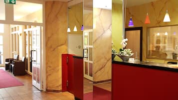 A hotel reception area with marble walls, a red reception desk, and a red carpet.