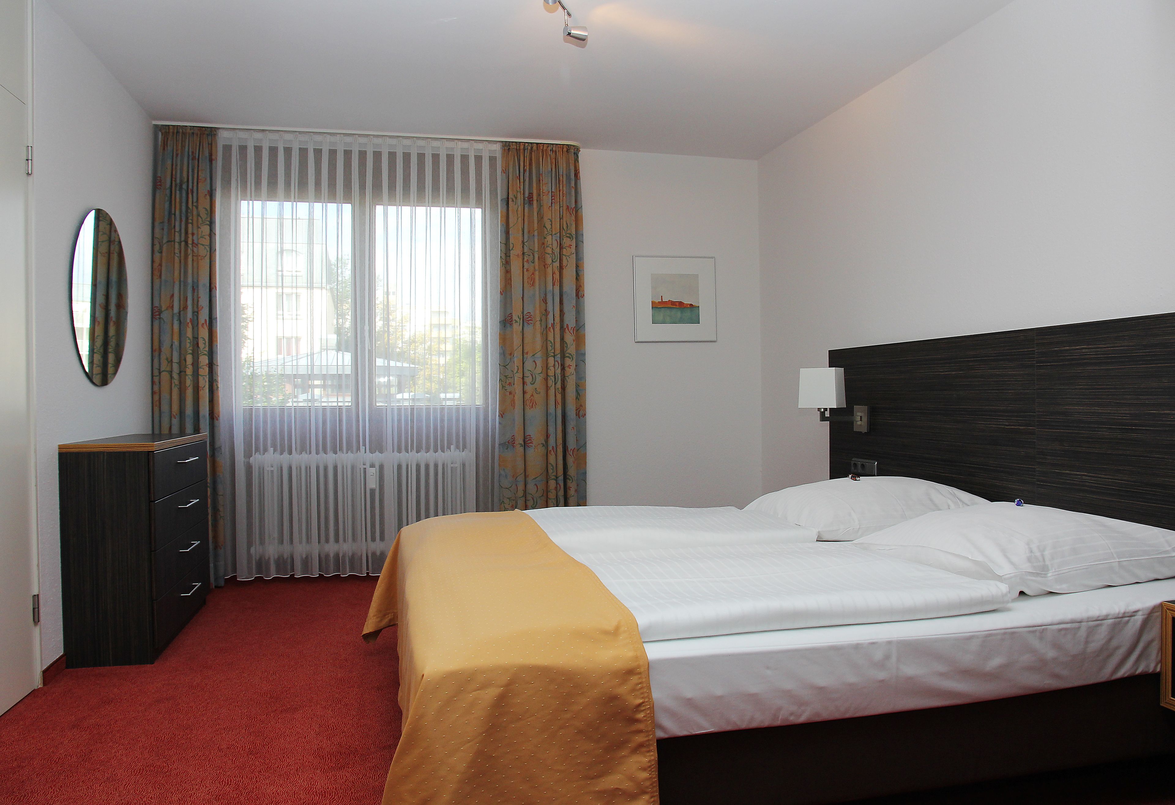A hotel room with a bed, a desk, and a window with curtains.