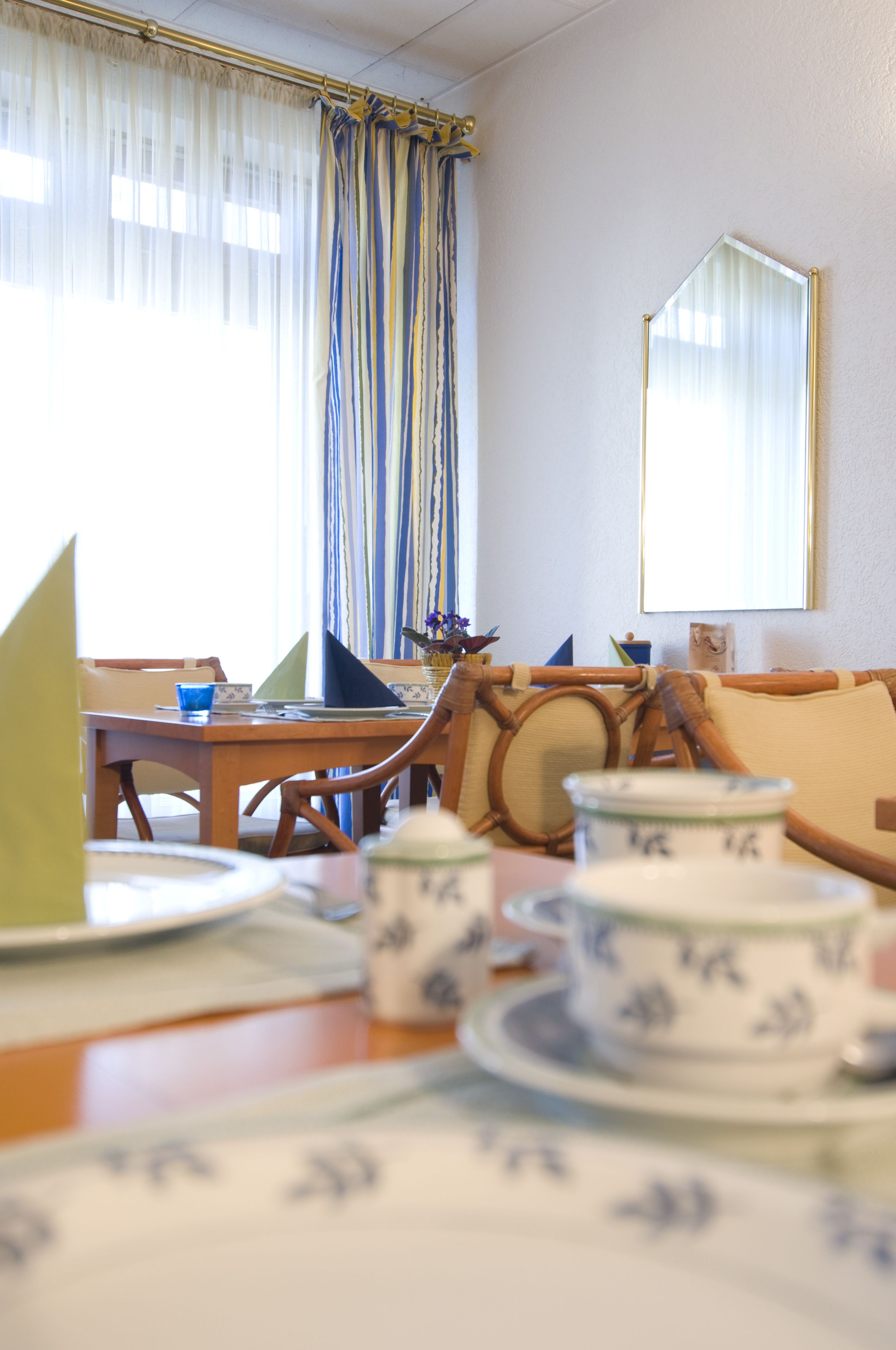 Een eethoek met een houten tafel gedekt voor twee personen, een bank en een raam met gordijnen.