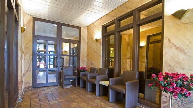 A lobby with a tiled floor, seating area with chairs and tables, and a potted plant with pink flowers.