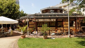 An outdoor café with tables and chairs, surrounded by potted plants and a clear sky.