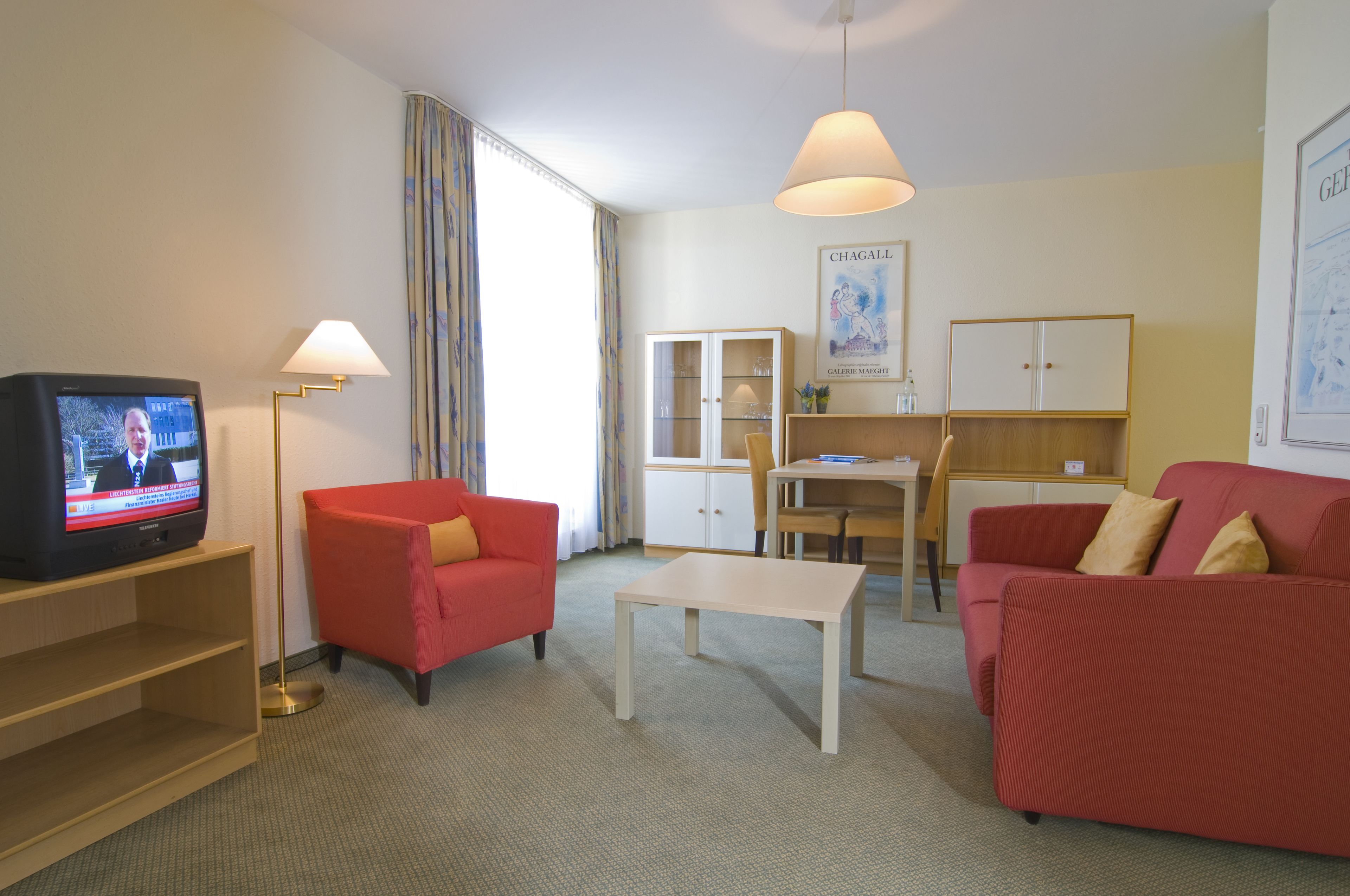 A living room with a television, red sofas, a coffee table, and a dining area with a table and chairs.